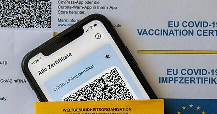 Ein Impfpass und ein Smartphone mit der CovPass-App liegen auf einem Impfzertifikat.