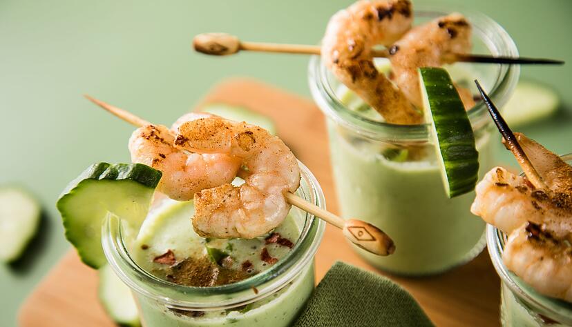 Eine kalte Suppe erfrischt an warmen Tagen - wie diese aus Gurken, Buttermilch und Basilikum, getoppt mit Garnelenspie&szlig;en, Chiliflocken und Cayennepfeffer.