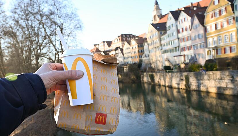 Eine McDonald's To-Go-T&uuml;te und ein To-Go-Becher werden auf der Neckarbr&uuml;cke in T&uuml;bingen vor der Kulisse der Altstadt gehalten (gestellte Szene).