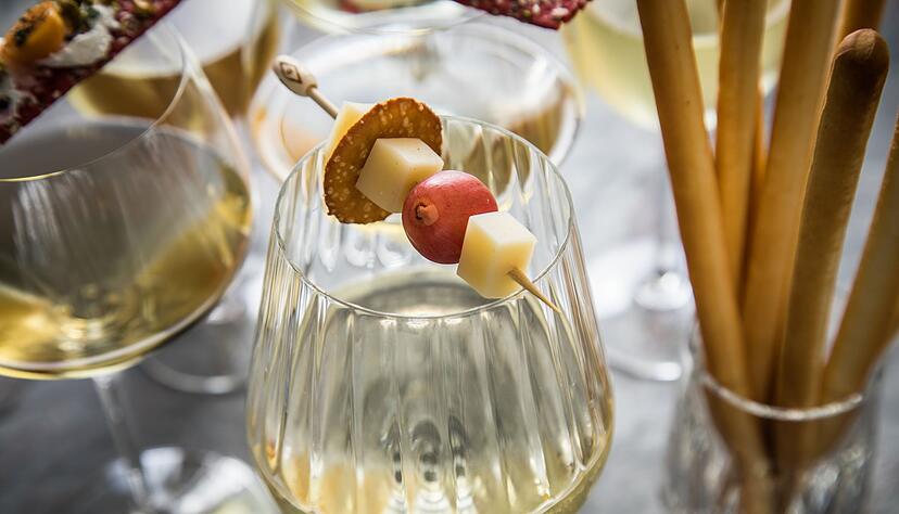 Weißwein mit Käsebegleitung: Kleine Spießchen auf dem Glasrand setzen Emmentaler und Co. in Szene. Spannend ist der Wechsel zwischen Käsehäppchen und Bretzel-Ring und Trauben.