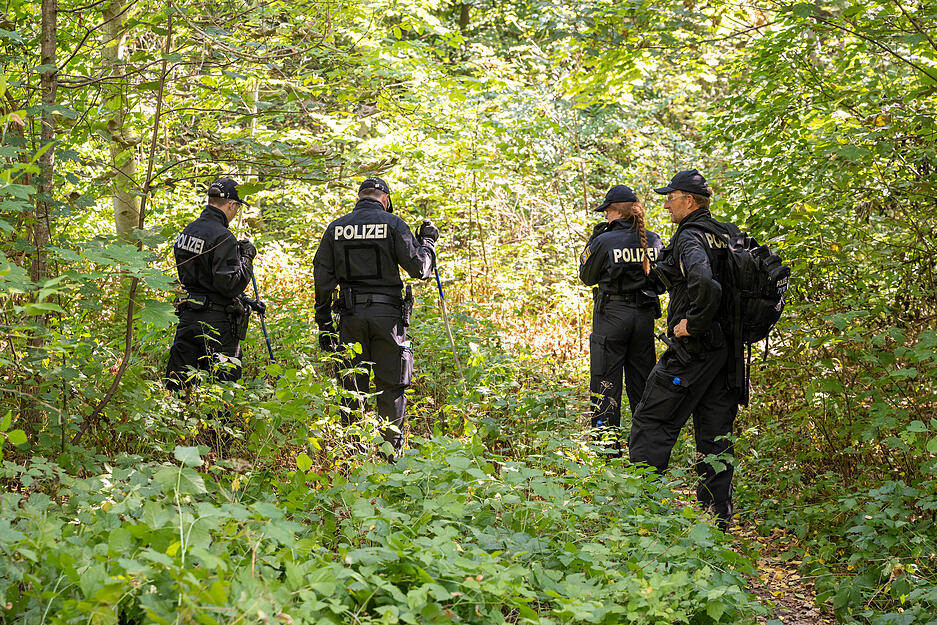 Polizisten durchsuchen ein Waldstück nach Spuren und Gegenständen, in dessen Nähe am 17.08.2022 eine weibliche Leiche in einem Auto entdeckt wurde.