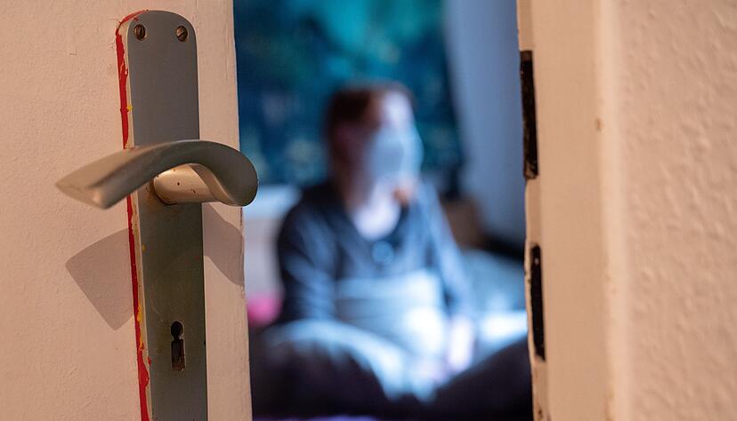 Eine Frau sitzt während der Isolation nach einem positiven Corona-PCR-Test auf ihrem Bett. Eine Frau sitzt während der Isolation nach einem positiven Corona-PCR-Test auf ihrem Bett.