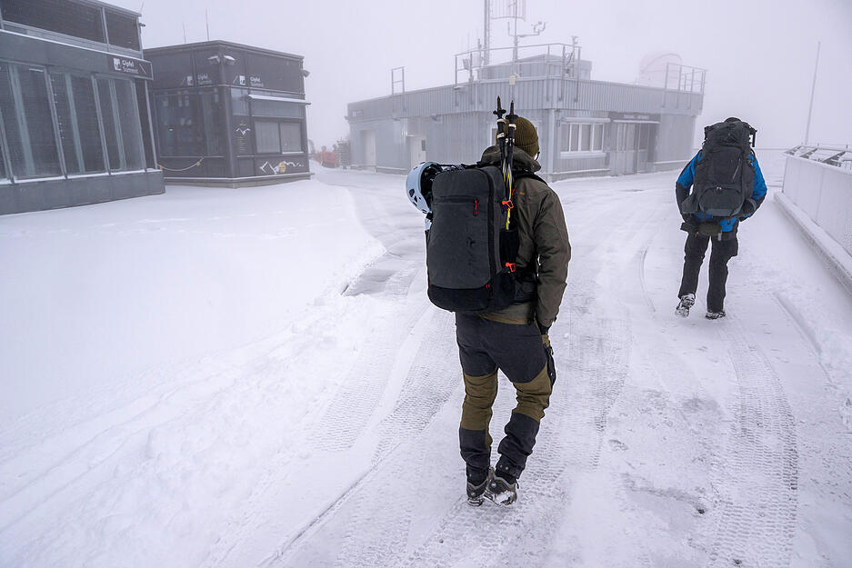 Zwei Bergsteiger laufen bei Schneefall über die Aufsichtsplattform der Zugspitze.