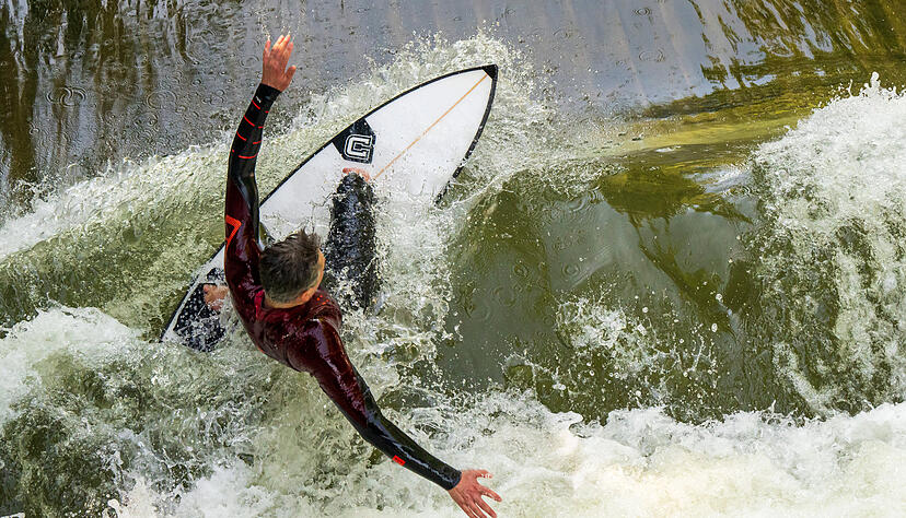 Ein Surfer reitet mit seinem Brett auf der Surfwelle Floßlände nahe der Isar im Süden der bayerischen Landeshauptstadt. +++ dpa-Bildfunk +++