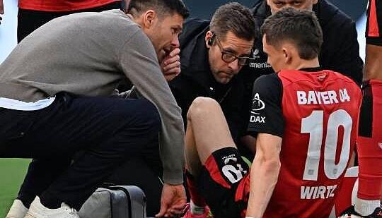 Leverkusens Trainer Xabi Alonso (l) spricht mit Florian Wirtz, der verletzt auf dem Platz sitzt. Leverkusens Trainer Xabi Alonso (l) spricht mit Florian Wirtz, der verletzt auf dem Platz sitzt.