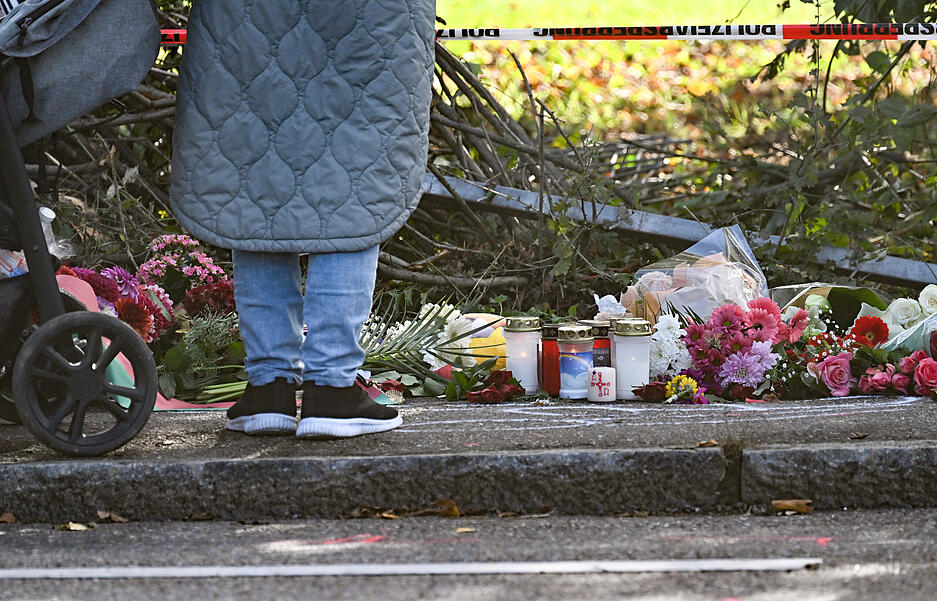 Eine Frau steht vor Blumen und Kerzen an der Unfallstelle in Esslingen auf einem Gehweg.