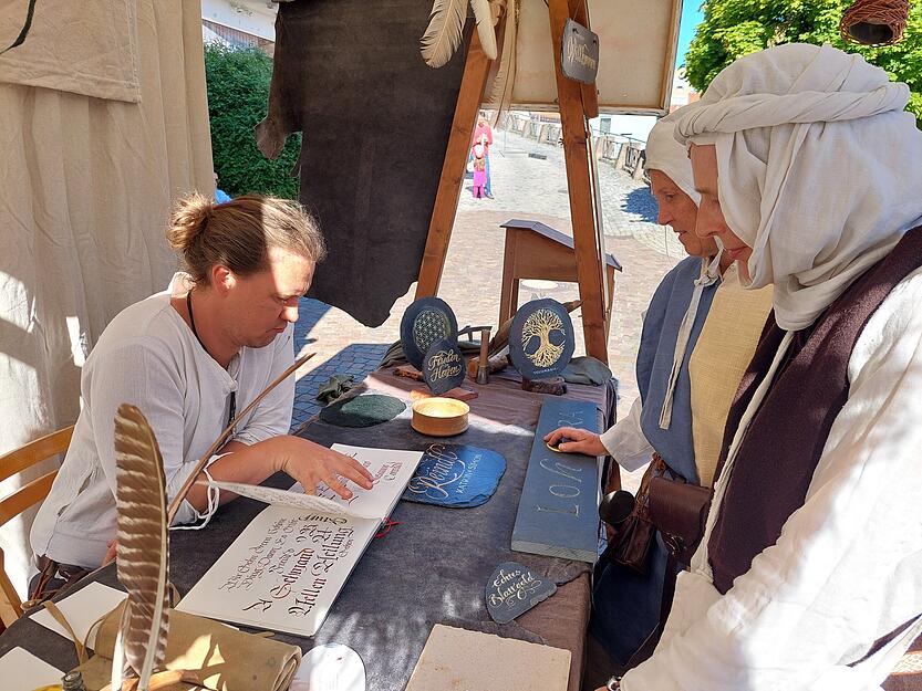 F&uuml;r die Arbeit von Kalligraf Sebastian Schulz aus Augsburg interessieren sich zwei mittelalterlich gewandete Damen in M&ouml;ckm&uuml;hl.