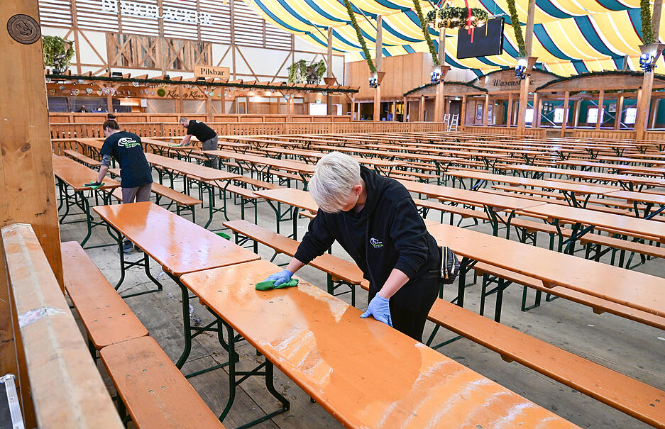 Mitarbeiterinnen in einem Festzelt reinigen zwei Tage vor der Eröffnung des 176. Cannstatter Volksfests Tische und Bänke.