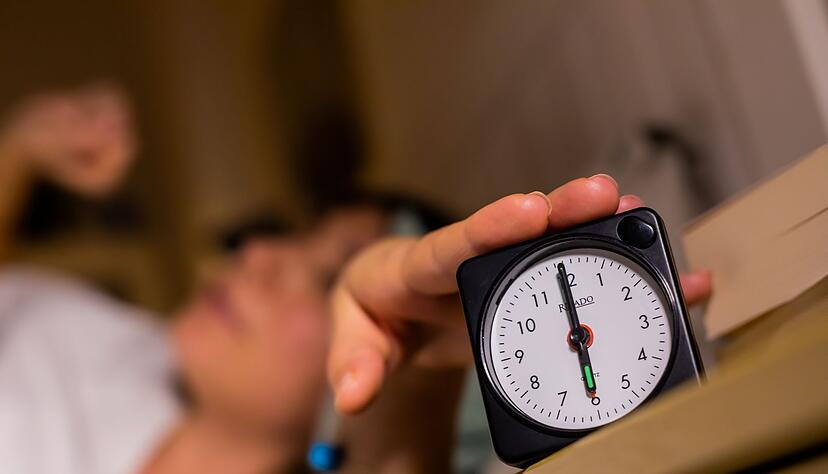 Eine Frau schaltet vom Bett aus einen auf sechs Uhr gestellten Wecker aus.