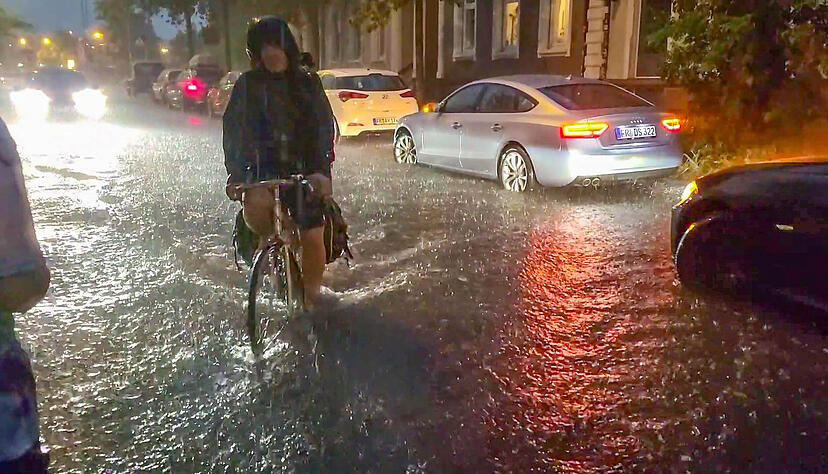 Ein Fahrradfahrer fährt in Freiburg über eine vom Regen überschwemmte Straße. Im August 2023 gab es hier ein schweres Unwetter. Ein Fahrradfahrer fährt in Freiburg über eine vom Regen überschwemmte Straße. Im August 2023 gab es hier ein schweres Unwetter.
