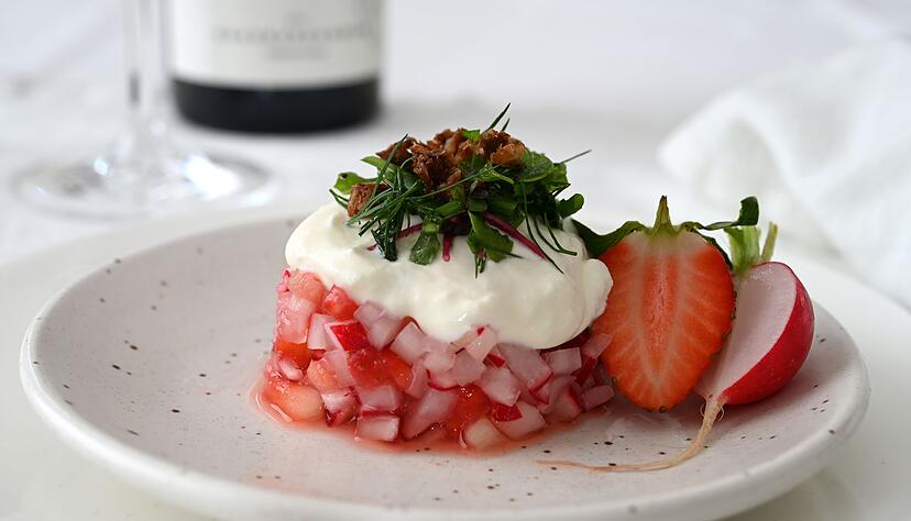 Der Erdbeer-Radieschen-Salat wird mit einem Servierring in Form gebracht. Darauf gibt es als Topping Ziegen-Feta-Creme, Kräutersalat und geröstete Krümel vom Schwarzbrot. Serviert wird er mit einem alkoholfreien Rosé.
