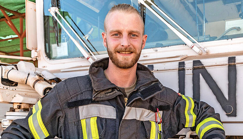 Oberfeldwebel Sebastian Witt tr&auml;gt im Einsatz in Mali neben seiner Milit&auml;runiform die &uuml;bliche Schutzkleidung f&uuml;r Feuerwehrleute. Hier steht er vor einem L&ouml;schfahrzeug der Vereinten Nationen, das sein Team nutzt.
Foto: Bundeswehr