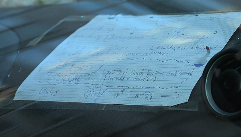 Ein Zettel mit handschriftlichen Notizen klebt auf dem Armaturenbrett eines beschädigten Fahrzeugs, das an einer Zufahrt zur Rheinbrücke steht.