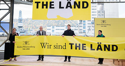 Nicole Hoffmeister-Kraut (CDU), Wirtschaftsministerin von Baden-Württemberg (v.l) Winfried Kretschmann (Bündnis 90/Die Grünen), Ministerpräsident von Baden-Württemberg, Ola Källenius, Vorstandsvorsitzender Daimler AG und die zwei Sterne Köchin Douce Steiner halten bei der Präsentation der Werbekampagne im Hafen von Stuttgart ein Transparent mit der Aufschrift "Wir sind "The Länd".