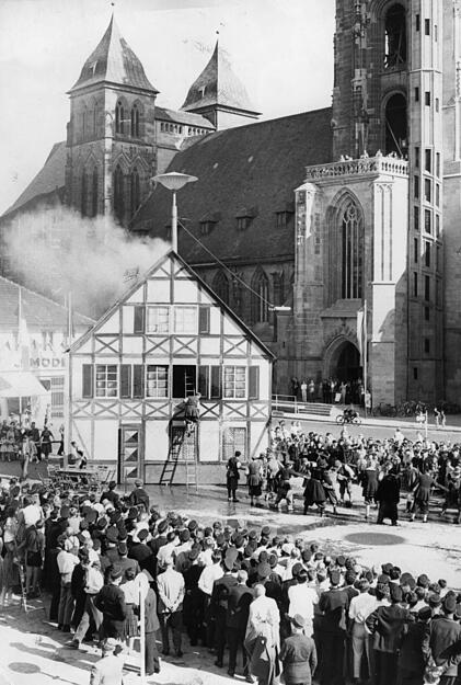 1963: Treffpunkt der Feuerwehren des Landes auf dem Heilbronner Marktplatz. Vor der Kulisse eines Fachwerkhauses zeigt die Stuttgarter Berufsfeuerwehr mit historischen Gewändern und Geräten, wie man früher einen Brand bekämpfte.