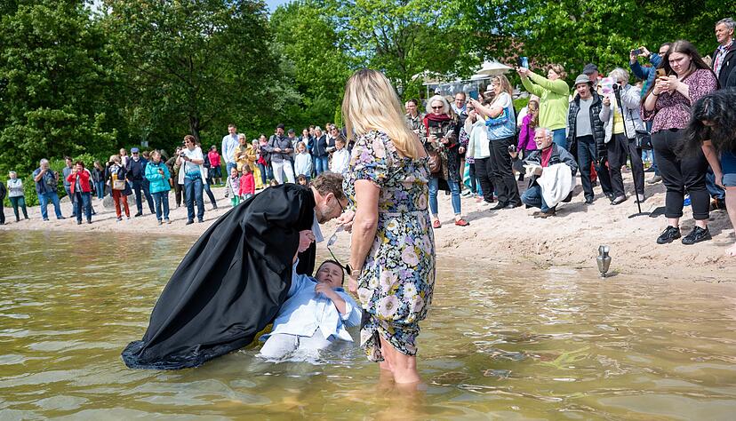 W&auml;hrend Pfarrer Gr&uuml;tzmacher vorsichtig Cailans Kopf ins Wasser taucht, h&auml;lt seine Mama die Brille trocken. Das Tauffest am Breitenauer See kommt gut an.