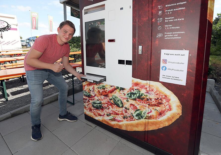 Andr&eacute; Endre&szlig; zieht eine fertige Pizza aus dem Ausgabeschlitz. Der Automat kann pro Bestellvorgang zwei Pizzen backen.