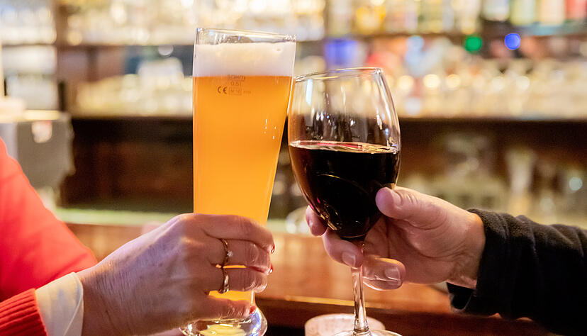 Zwei Gäste stoßen in einer Gaststätte mit Wein und Bier an.