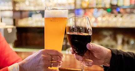 Zwei Gäste stoßen in einer Gaststätte mit Wein und Bier an.