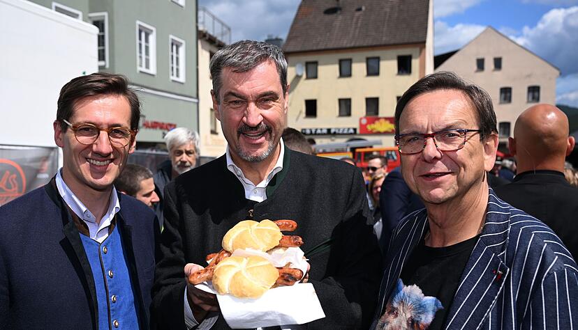 Markus Söder (M.) hält Bratwurst-Semmeln in die Kamera.
