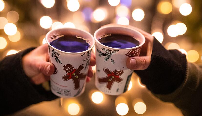 Zwei Besucherinnen eines Weihnachtsmarktes stoßen mit Glühwein an.