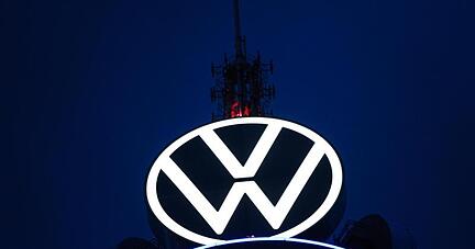 Das Volkswagen Logo leuchtet auf dem VW-Tower vor dunklem Himmel.