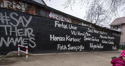 Ein kleines Mädchen schaukelt vor der Wand eines Jugendzentrums, auf dem die Namen der Opfer des Anschlags vom 19. Februar geschrieben stehen.