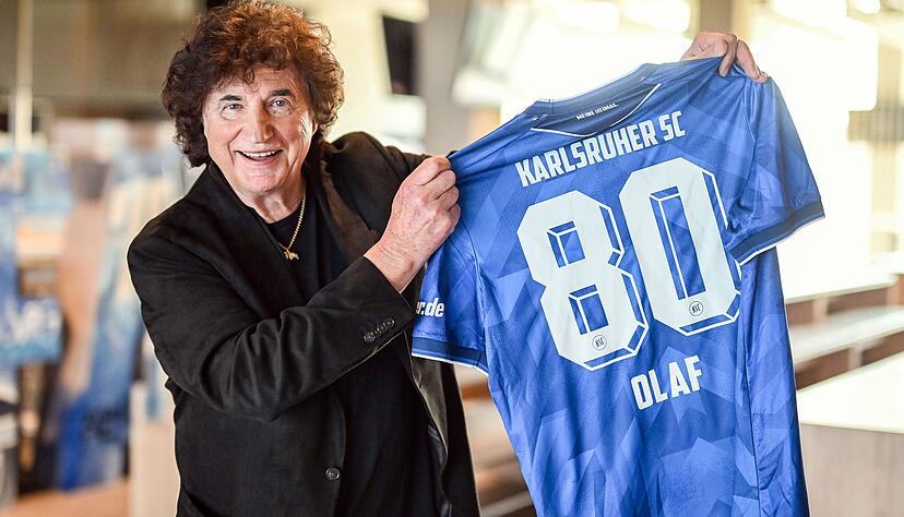 Olaf Malolepski, h&auml;lt im BBBank Wildpark ein Trikot des Zweitbundesligisten Karlsruher SC in seinen H&auml;nden. Auf dem Trikot steht &bdquo;Karlsruher SC - 80 Olaf. Malolepski hat am 27.03.2026 seinen 80. Geburtstag. Er war S&auml;nger bei der l&auml;ngst aufgel&ouml;sten Schlagerband Flippers. Seit Jahren ist er erfolgreicher Solok&uuml;nstler.