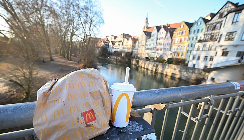 Eine McDonald's To-Go-T&uuml;te und ein To-Go-Becher werden auf der Neckarbr&uuml;cke in T&uuml;bingen vor der Kulisse der Altstadt gehalten (gestellte Szene).