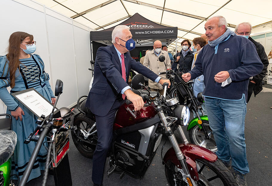 Harry Mergel (Mitte) probiert beim Rundgang zusammen mit Käthchen Daphne Schietinger ein Motorrad mit Elektroantrieb aus.