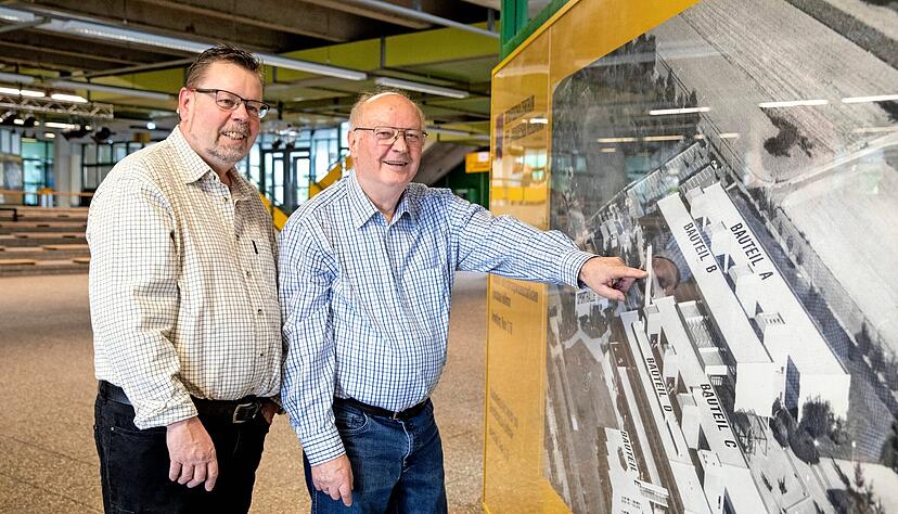 Der aktuelle Hausmeister Dirk Wolf (links) mit seinem Vater und Vorg&auml;nger Karl-Heinz Wolf in der Aula vor einer Luftaufnahme des Kreisberufsschulzentrums.