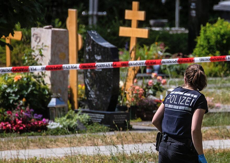 Eine Polizistin geht über den abgesperrten Teil an einem Tatort auf einem Friedhof. Durch den Wurf eines explodierenden Gegenstands auf eine Trauergemeinde gab es mehrere Verletzte. Eine Polizistin geht über den abgesperrten Teil an einem Tatort auf einem Friedhof. Durch den Wurf eines explodierenden Gegenstands auf eine Trauergemeinde gab es mehrere Verletzte.