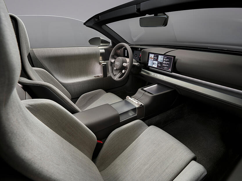 Im Audi Concept C sitzt man sehr tief. Das komplett lederfreie Interieur ist wie die Außenhaut aufs Wesentliche reduziert. Das fahrerorientierte Cockpit verfügt über ein Display hinter dem Lenkrad. Ein weiterer 10,4-Zoll-Bildschirm fährt bei Bedarf aus und ist zentral in der Mitte platziert.