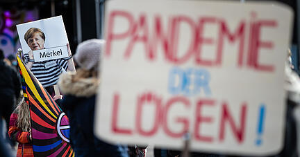 &laquo;Pandemie der L&uuml;gen!&raquo; steht auf dem Schild eines Teilnehmers geschrieben, der an einer Demonstration gegen die Corona-Politik der Bundesregierung in G&ouml;ppingen teilnimmt. Im Hintergrund ist ein Schild zu sehen, auf dem Bundeskanzlerin Merkel in &laquo;Str&auml;flingskleidung&raquo; abgebildet ist. Foto: dpa