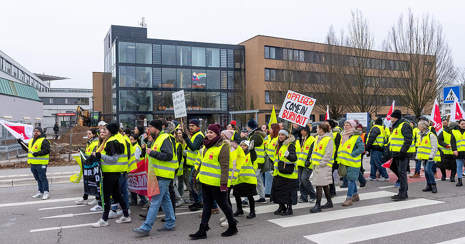 Mit Warnwesten und Schildern ausgestattet ziehen die streikenden Pflege-Mitarbeiter durch Heilbronn.