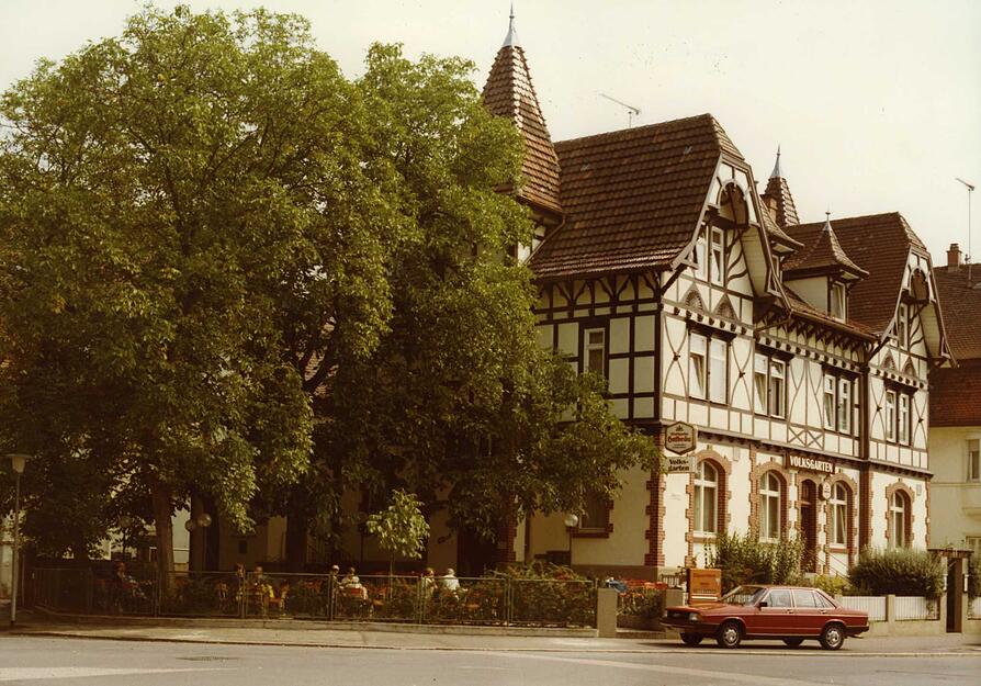 Ansicht des Fachwerkhauses. Im Aufnahmejahr wurde es unter Denkmalschutz gestellt. Unter den Schatten spendenden Bäumen befindet sich die angrenzende Gartenwirtschaft des Volksgartens mit 85 Plätzen und Seiteneingang. Aufnahme aus dem Jahr 1992.