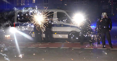 Polizeibeamte stehen in der Silvesternacht hinter explodierendem Feuerwerk.