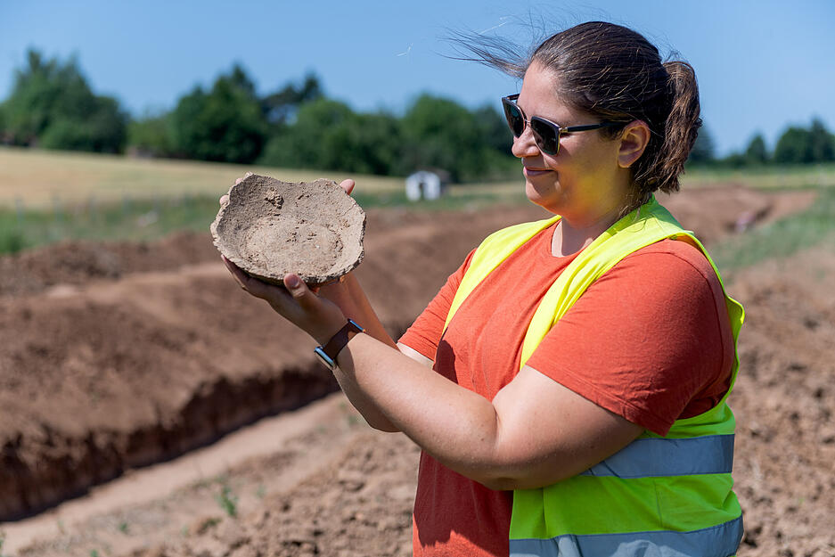 Grabungsleiterin Rebecca Bunge präsentiert stolz ein Bodenfragment eines Keramikgefäßes.