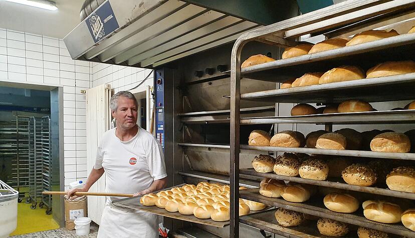 Bäckermeister Roland Bürk holt frisch gebackene Brötchen mit einem Holzschieber aus dem Ofen. Der Arbeitsschritt ist Teil der morgendliche Routine in der Backstube. Foto: Möllers