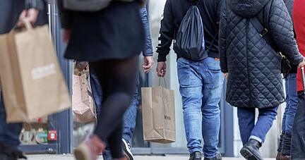 Menschen gehen mit ihren Einkaufstaschen auf einer Straße entlang.