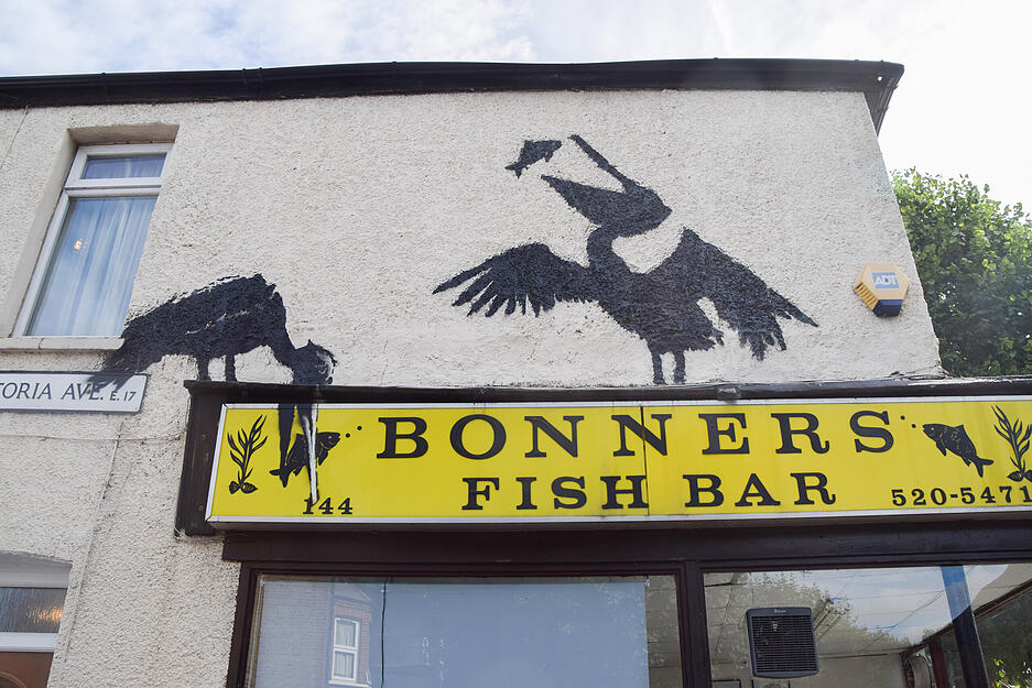 Neues Banksy-Kunstwerk, das ein Paar Pelikane zeigt, die &uuml;ber einem Fish-and-Chips-Laden Fisch essen.