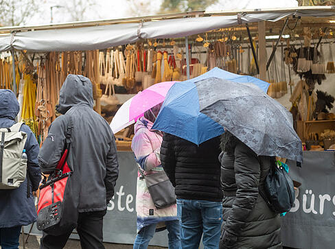 Mit Regenschirmen oder Kapuzen wagen sich einige Besucher &uuml;ber den Heilbronner Pferdemarkt am Samstag.