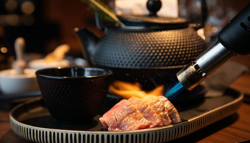Vier d&uuml;nne Scheiben vom Wagyu-Beef werden mit dem Flambierbrenner anger&ouml;stet.