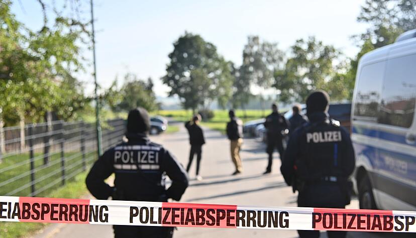 Einsatzkräfte der Polizei stehen hinter einer Polizeiabsperrung nach einer Razzia in Hesselbronn. Einsatzkräfte der Polizei stehen hinter einer Polizeiabsperrung nach einer Razzia in Hesselbronn.