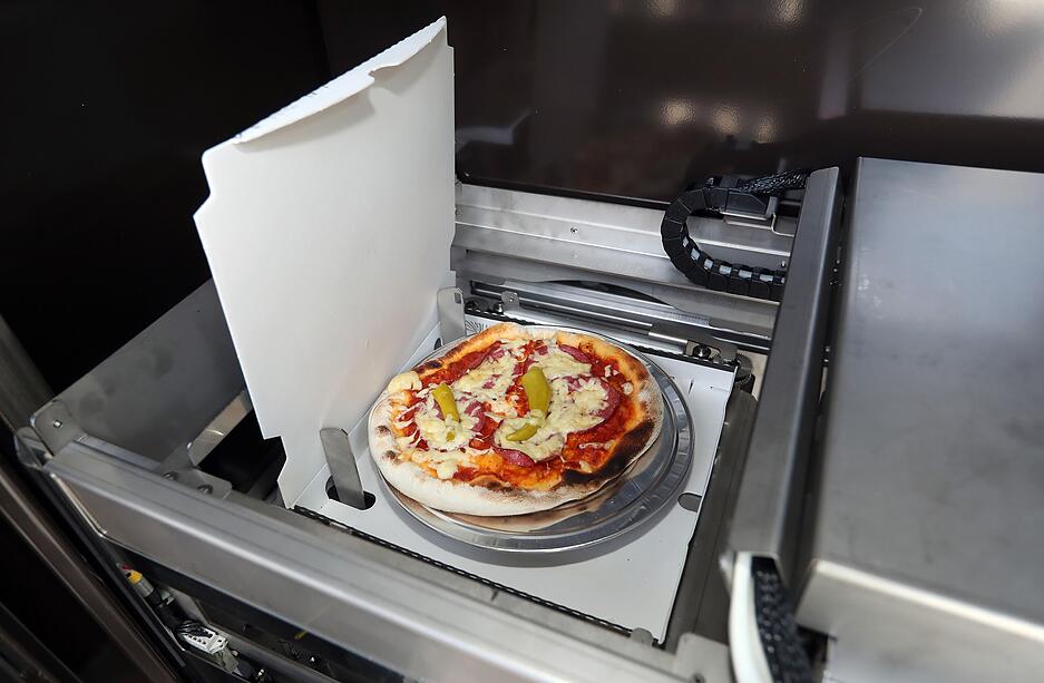Blick ins Innere des Automaten. Die gew&auml;hlte Pizza ist aus der K&uuml;hleinheit, die sich auf der R&uuml;ckseite befindet, automatisch in den Ofen gefahren worden.