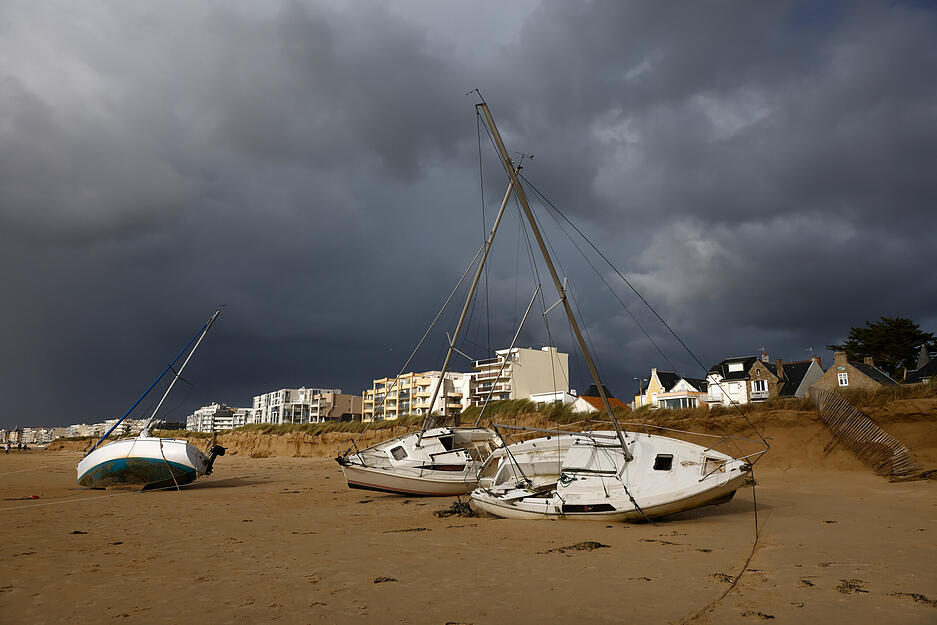 Angeschwemmte Boote liegen am Strand in der Bretagne im Sand.