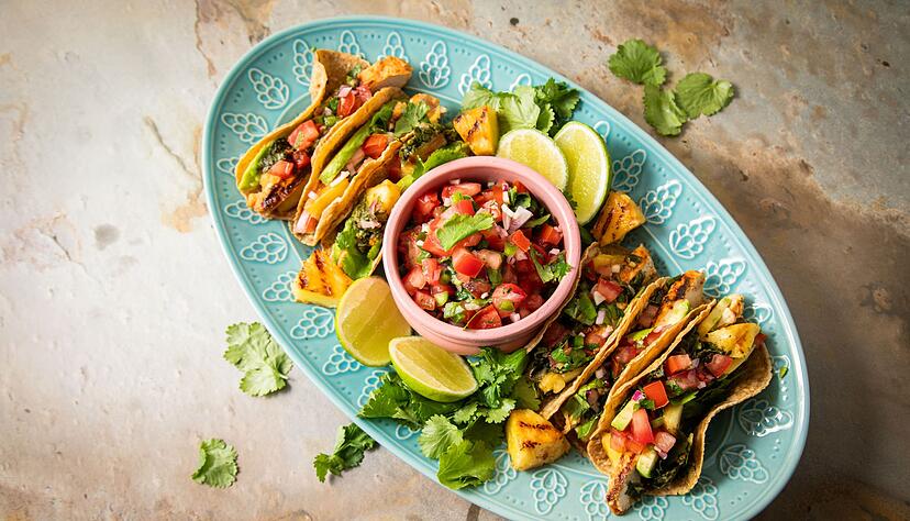 Richtig stilecht werden Hähnchen-Tacos erst mit Zugaben wie der mexikanische Tomatensalsa «Pico de Gallo», argentinischer Kräutersauce «Chimichurri», Avocado, gegrillter Ananas, Koriander und Limetten.