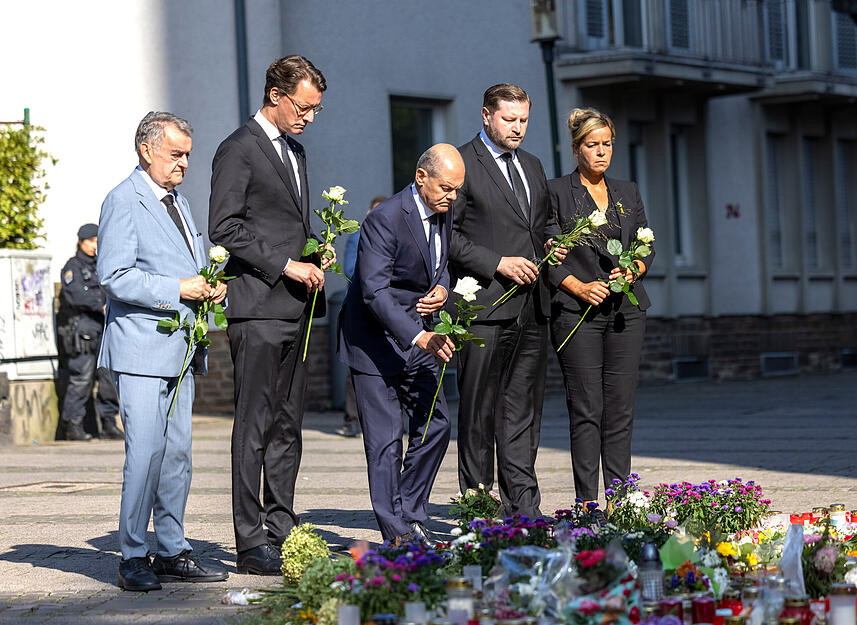 Herbert Reul (CDU, l-r), Innenminister von Nordrhein-Westfalen, Hendrik Wüst (CDU), Ministerpräsident von Nordrhein-Westfalen, Bundeskanzler Olaf Scholz (SPD), Tim Kurzbach (SPD), Bürgermeister von Solingen, und Mona Neubaur (Grüne), stellvertretende Ministerpräsidentin, legen Blumen an einer Kirche in der Nähe des Tatorts ab.
