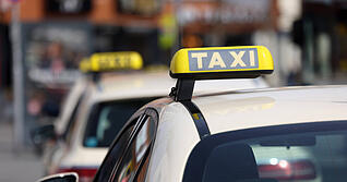 Taxis warten vor einem Hauptbahnhof auf Fahrg&auml;ste. Taxi-Logos auf den D&auml;chern der Fahrzeuge. (Symbolbild)