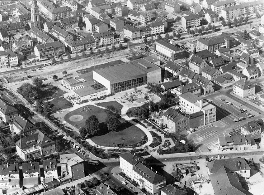 Die Luftaufnahme von 1960 zeigt die Anlage der Heilbronner Festhalle Harmonie entlang der Allee, mit den dazugehörigen Parkplätzen und die geschickte Gestaltung des Stadtgartens. Rechts, etwas zurückgesetzt, ist das Gebäude der Vereinsdruckerei sichtbar.